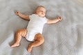 Top view of baby lying on a bed on grey blanket sleeping in a bright room, spreading hands aside, keeping eyes closed Royalty Free Stock Photo