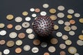 A painted ball like a SARS-CoV-2 virion on the middle of many coins from different countries