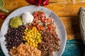 Top-view of a barbacoa burrito bowl, meat rice black beans sour cream guacamole chopped vegetables