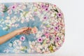 Top view of bath filled with blue bubble water, flowers and petals with woman`s hand Royalty Free Stock Photo