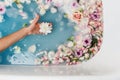 Top view of bath filled with blue bubble water and petals with woman`s hand