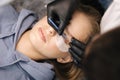 Top view of beautician making eyelash lamination procedures for young blond hair model. Professional beauty studio