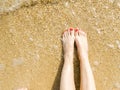 Top view of beautiful female feet with bright red pedicure on the sand of the beach. The sea wave washes women`s feet Royalty Free Stock Photo