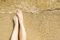 Top view of beautiful female feet with bright red pedicure on the sand of the beach. The sea wave washes women`s feet Royalty Free Stock Photo