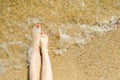 Top view of beautiful female feet with bright red pedicure on the sand of the beach. The sea wave washes women`s feet Royalty Free Stock Photo