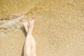 Top view of beautiful female feet with bright red pedicure on the sand of the beach. The sea wave washes women`s feet Royalty Free Stock Photo