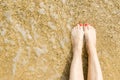 Top view of beautiful female feet with bright red pedicure on the sand of the beach. The sea wave washes women`s feet Royalty Free Stock Photo