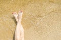 Top view of beautiful female feet with bright red pedicure on the sand of the beach. The sea wave washes women`s feet Royalty Free Stock Photo