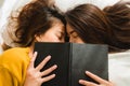 Top view of beautiful young asian women lesbian happy couple kiss and smiling while lying together in bed under book at home. Royalty Free Stock Photo