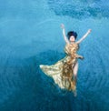 Top view of a beautiful young sexy mermaid woman in golden evening dress, floating weightless elegant swimming in the blue,
