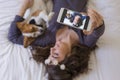 Top view of a beautiful young woman taking a selfie with mobile phone on bed with her cute small dog besides. Home, indoors and Royalty Free Stock Photo