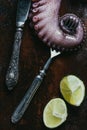 top view of big octopus tentacle with fork, knife and limes on rusty Royalty Free Stock Photo
