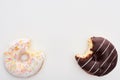 Top view of bitten glazed chocolate and white doughnuts on white background .