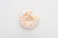 Top view of bitten white delicious doughnut with sprinkles on white background.