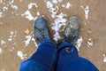 top view of black boots and legs in blue jeans all covered in mud standing on dirty ground covered with snow. Concept of leaving