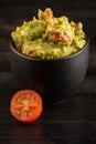 Top view of black bowl with guacamole on dark table with half a small tomato Royalty Free Stock Photo