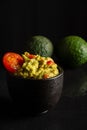 Top view of black bowl with guacamole on glossy black background with avocados, selective focus Royalty Free Stock Photo