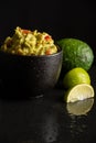 Top view of black bowl with guacamole on wet table with reflection of lime and avocado, selective focus, black background, Royalty Free Stock Photo