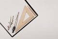 Top view of black clipboard, white blank, triangle ruler, compasses and pencil on white background.