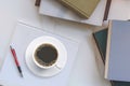 Top view of black Coffee in white ceramic Cup with pen on Book and group of old textbooks stacked on marble Table