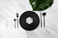 Top view of black cutlery and black plate on white marble background. Table setting flat lay with tropical monstera leaf. Royalty Free Stock Photo