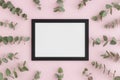 Top view of a black frame mockup surrounded by branches of eucalyptus on a pink background