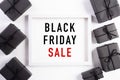 Top view of Black Friday Sale text on white picture frame with black gift box and Christmas ball and berries on white background. Royalty Free Stock Photo