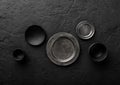Top view of black and grey empty plates and bowls on black stone background