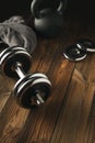 Top view of black iron kettlebell, dumbbell and grey towel on wooden floor Sport background with copyspace