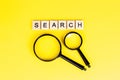 Top view of black magnifying glass with the word search on light yellow background. Royalty Free Stock Photo