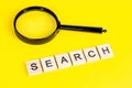 Top view of black magnifying glass with the word search on light yellow background. Royalty Free Stock Photo