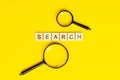 Top view of black magnifying glass with the word search on light yellow background. Royalty Free Stock Photo