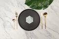 Top view of black plate and gold cutlery on white marble background. Luxury table setting flat lay. Royalty Free Stock Photo