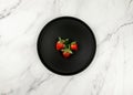 Top view of black plate on white marble background. Three strawberries flat lay. Royalty Free Stock Photo