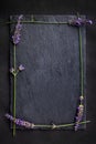 Top view of a black slate board with four lavender flowers around as a frame on a dark background.