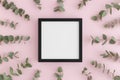 Top view of a black square frame mockup surrounded by branches of eucalyptus on a pink background