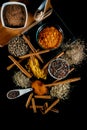 Top view of a black table with lots of spices on top, cinnamon twigs, peppercorns and ground spices. Concept of gastronomic