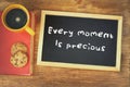 Top view of blackboard with the phrase every moment is precious next to coffee cup over wooden table Royalty Free Stock Photo