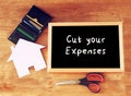 Top view of blackboard with the slogan cut your expenses scissors, wallet with credit cards and house shaped paper. household or