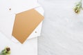 Top view of blank gold card in white envelop with pine leaf on t