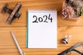 Top view of 2024 blank list on table with small airplane, light bulb, pen, succulent plant and glasses. New year goals and