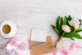 Top view of blank note, kraft envelope, coffee cup and peony flowers over white wood rustic background.Copy space.