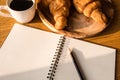 Top view of blank notebook with pencil, croissant and coffee on wooden table background. Royalty Free Stock Photo