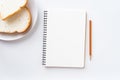 Top view of blank notebook on the table. bread in a plate and pencil on a white ground