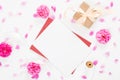 Top view blank paper card, red envelope, gift box, rose flowers buds and petals on white background. Minimal flat lay style Royalty Free Stock Photo