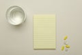 Top view of blank yellow note paper, capsule pills and glass of water on the bright desk