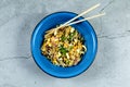 Top view of a blue ceramic bowl containing rice, corn, and salad with chopsticks on it