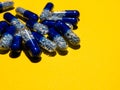 Top view of blue, semi transparent pills with white and pale blue medicine pellets on yellow background with space for text or Royalty Free Stock Photo