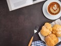 Top view of a book with choux cream on a plate and a white coffee cup on a table. Royalty Free Stock Photo