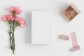 Top view of a book mockup with a bouquet of pink carnations and workspace accessories on a white table